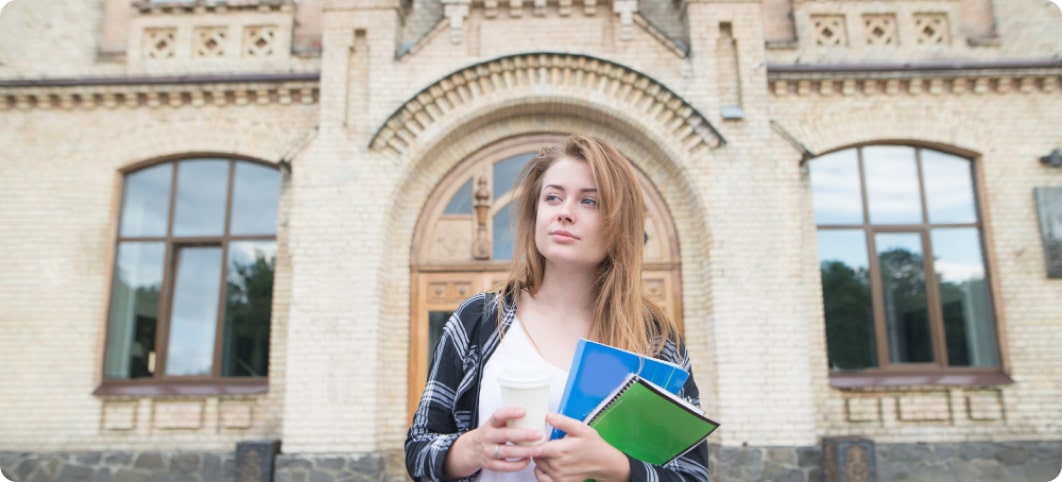 A girl takes a book in her hand and stands outside a university